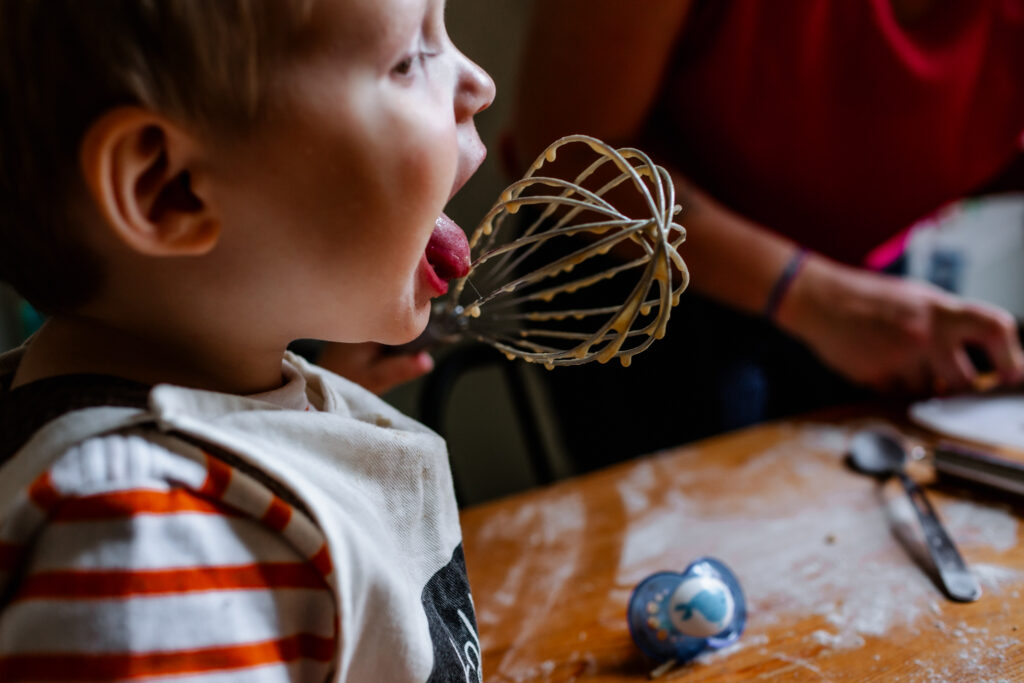 Little boy licking a whisk while preparing some Christmas cookies