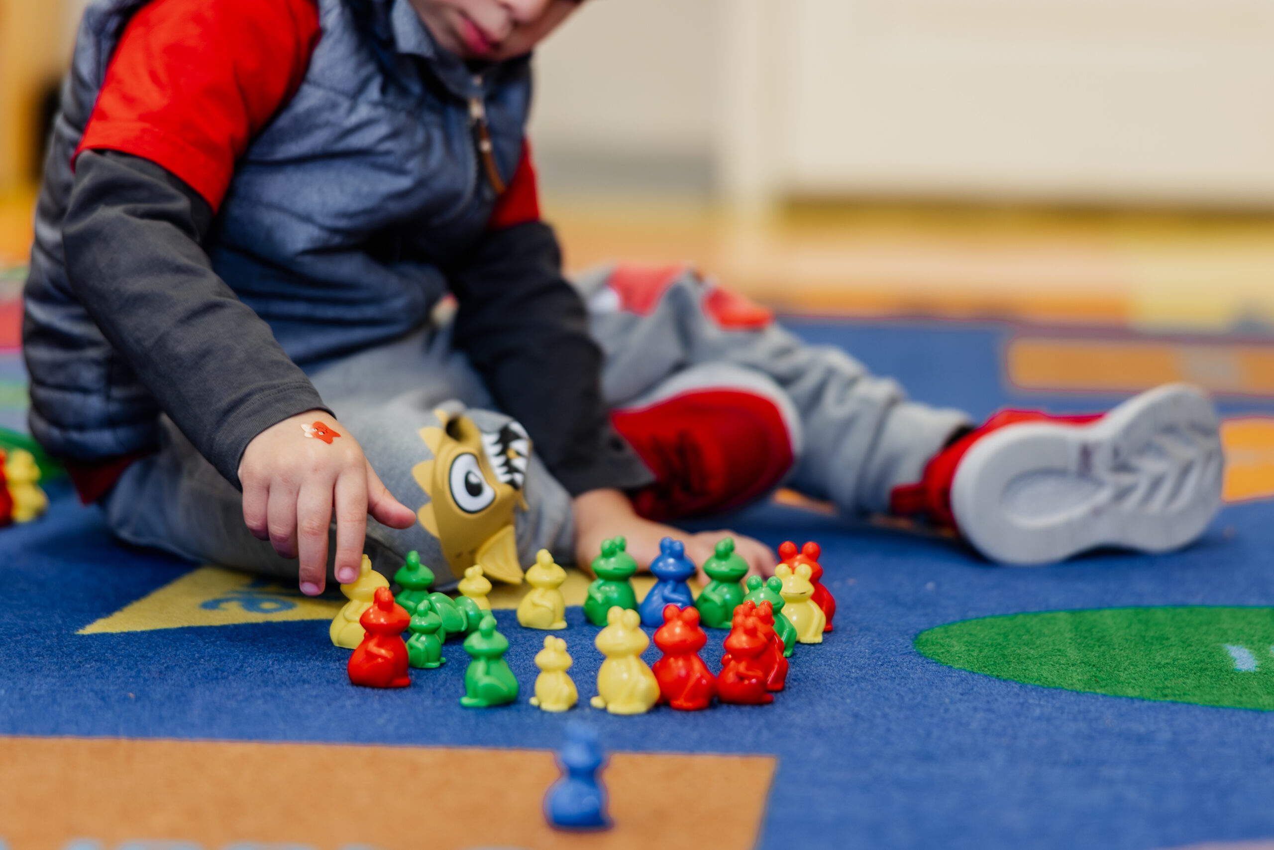 保育施設のカーペットでカエルのおもちゃを並べる男の子